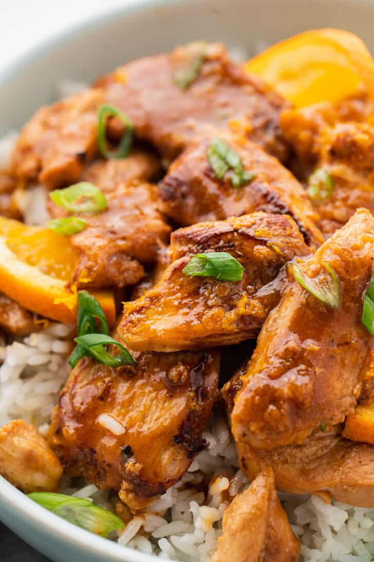 Closeup on the best orange chicken recipe garnished with green onions, over white rice.