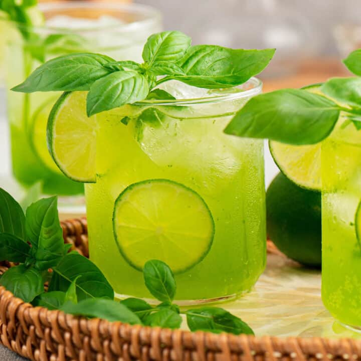 Green hued basil cocktails garnished with lemon on a wicker tray.