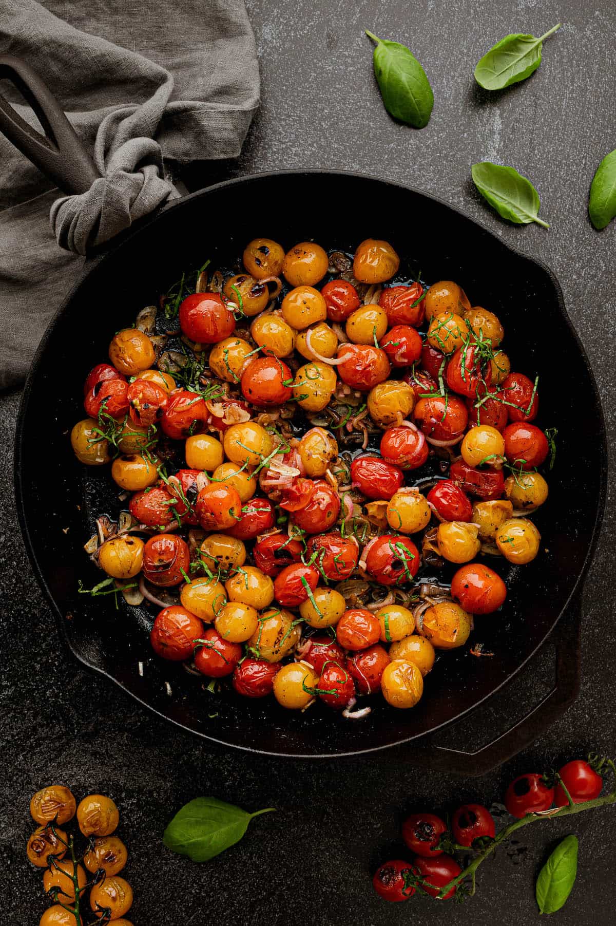 Large cast iron skillet filled with red and yellow summer fruit, shallots and basil.