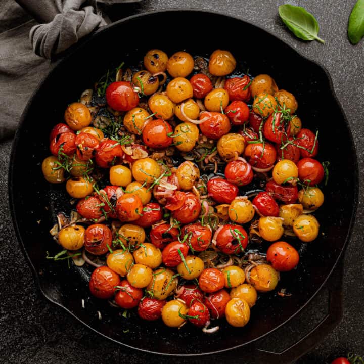 Large cast iron skillet filled with blistered tomatoes, shallots and basil.