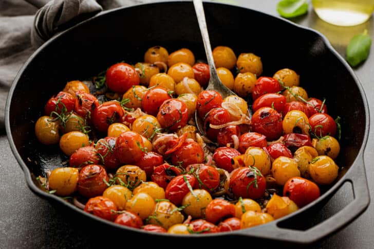 Red and yellow blistered cherry tomatoes with shallots and basil, in a cast iron skillet.