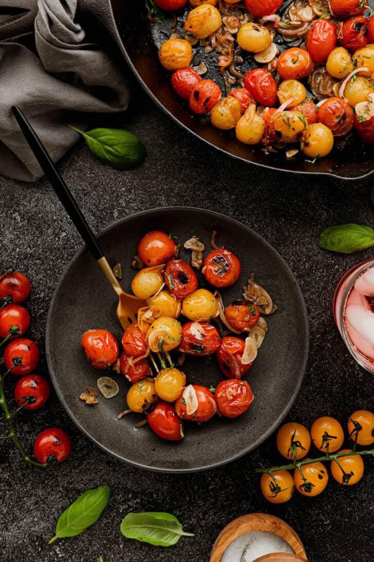 A small dark plate of blistered grape tomatoes with shallot, garlic and basil.