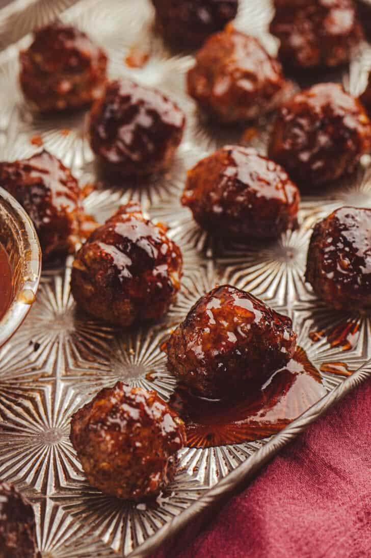Small balls of cooked ground meat on a textured baking pan glazed with a deep red glossy sauce.