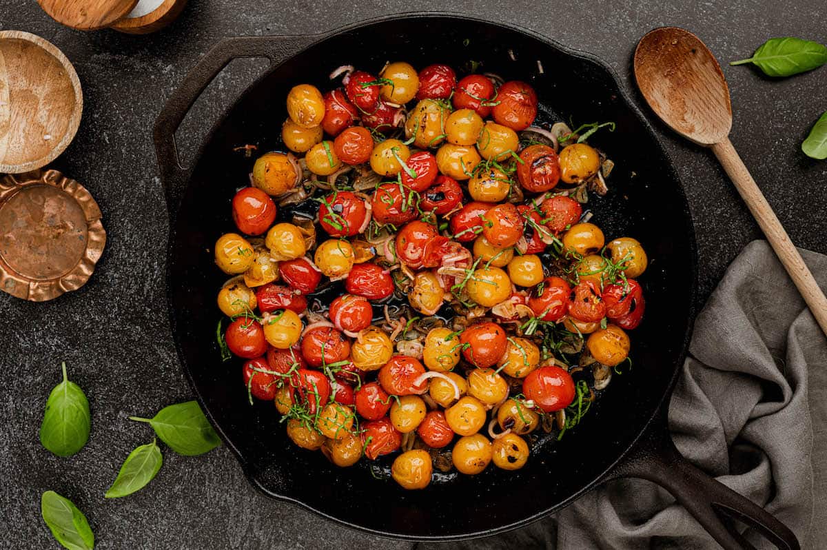 Sauteed tomatoes sprinkled with sliced basil in a cast iron skillet.