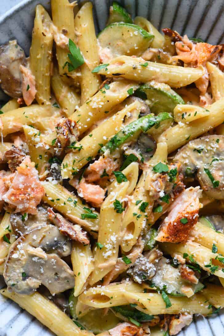 Penne noodles in a creamy sauce with zucchini, mushrooms, chunks of pink fish, and sundried tomatoes, garnished with Parmesan cheese and parsley.