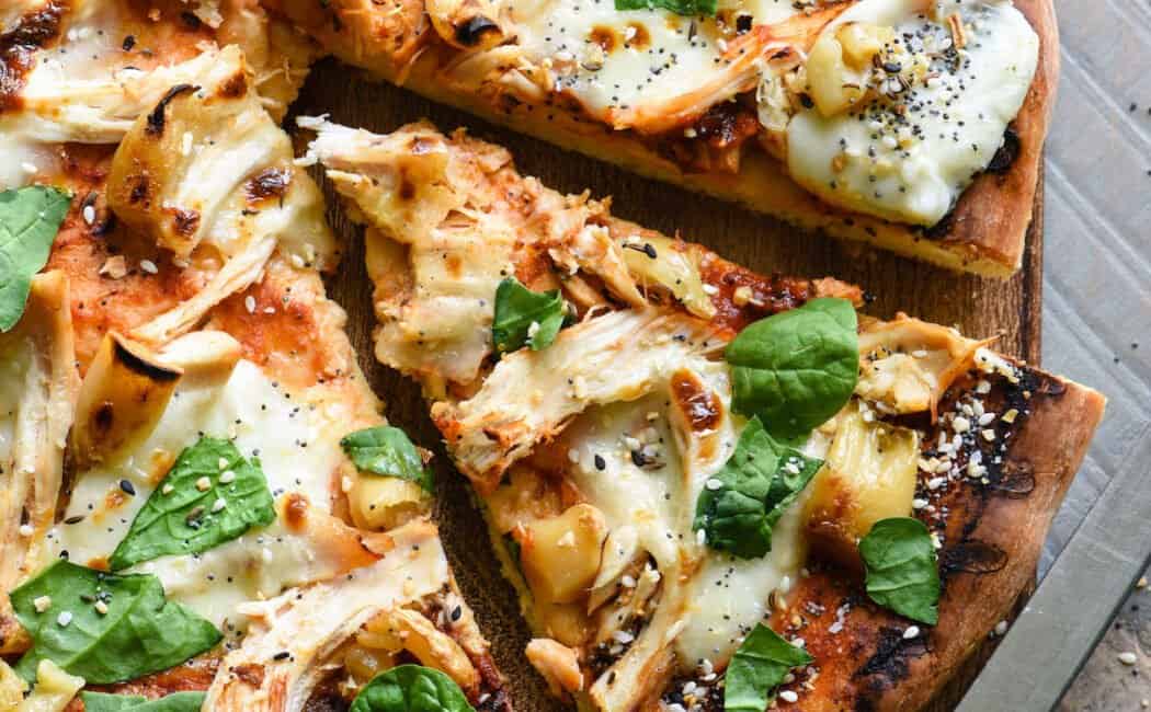 A round chicken pizza with roasted garlic and basil on a wooden cutting board.
