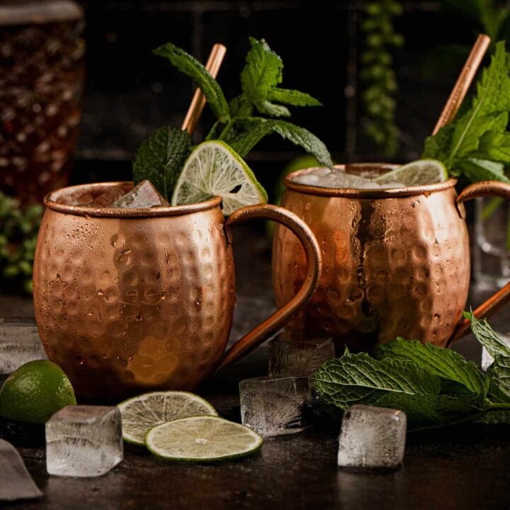 Two hammered copper mugs filled with Moscow mules with whiskey, garnished with limes and mint.