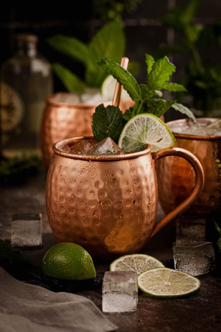 Two hammered copper mugs filled with a Kentucky mule cocktail, garnished with lime wedges and mint sprigs.