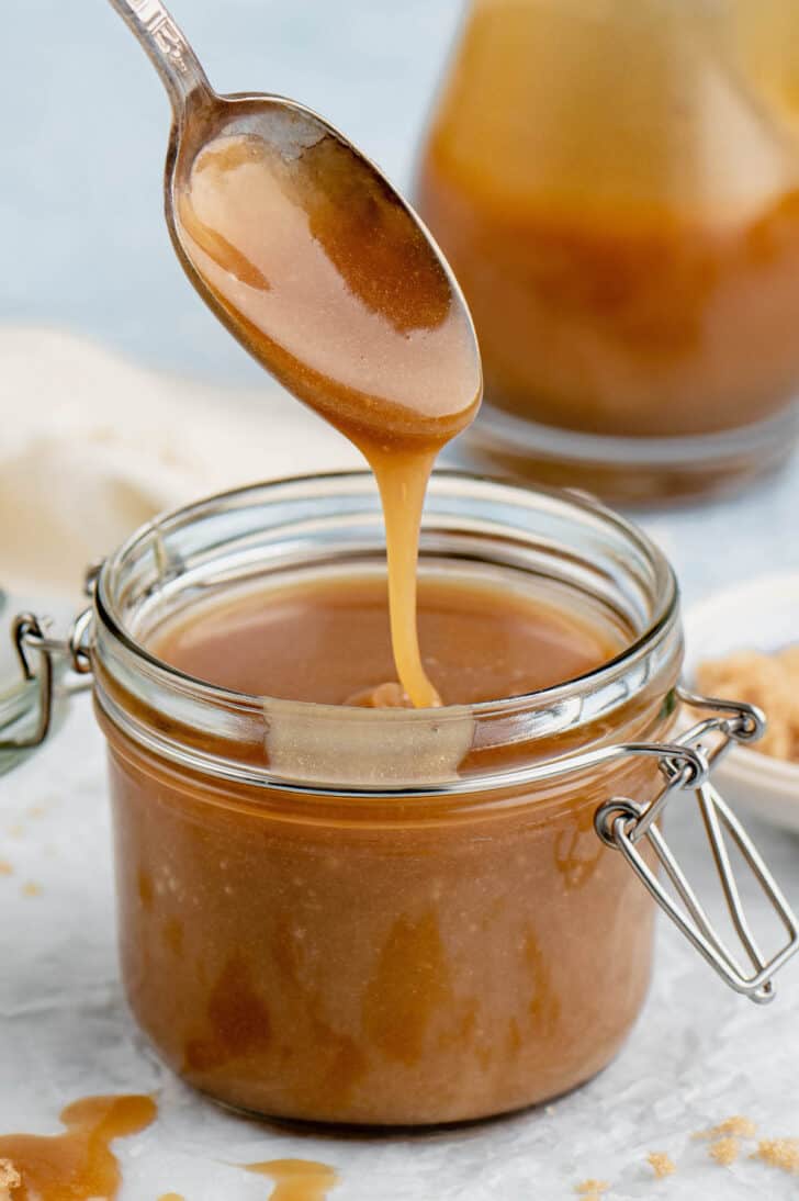 A spoon drizzling microwave caramel sauce into a small glass jar.