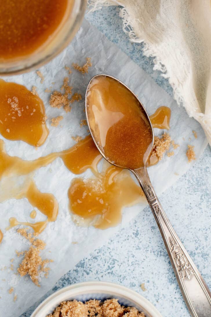 A small spoon smearing caramel over a light surface studded with brown sugar.