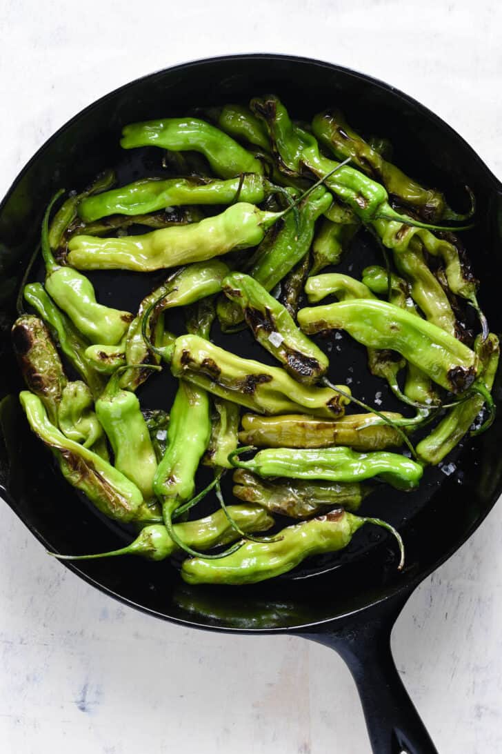 Blistered green vegetables sprinkled with flaky sea salt in a cast iron skillet.