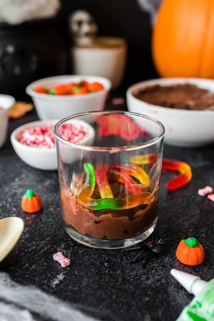 A small glass filled with a layer of chocolate pudding topped with a few gummy worms.