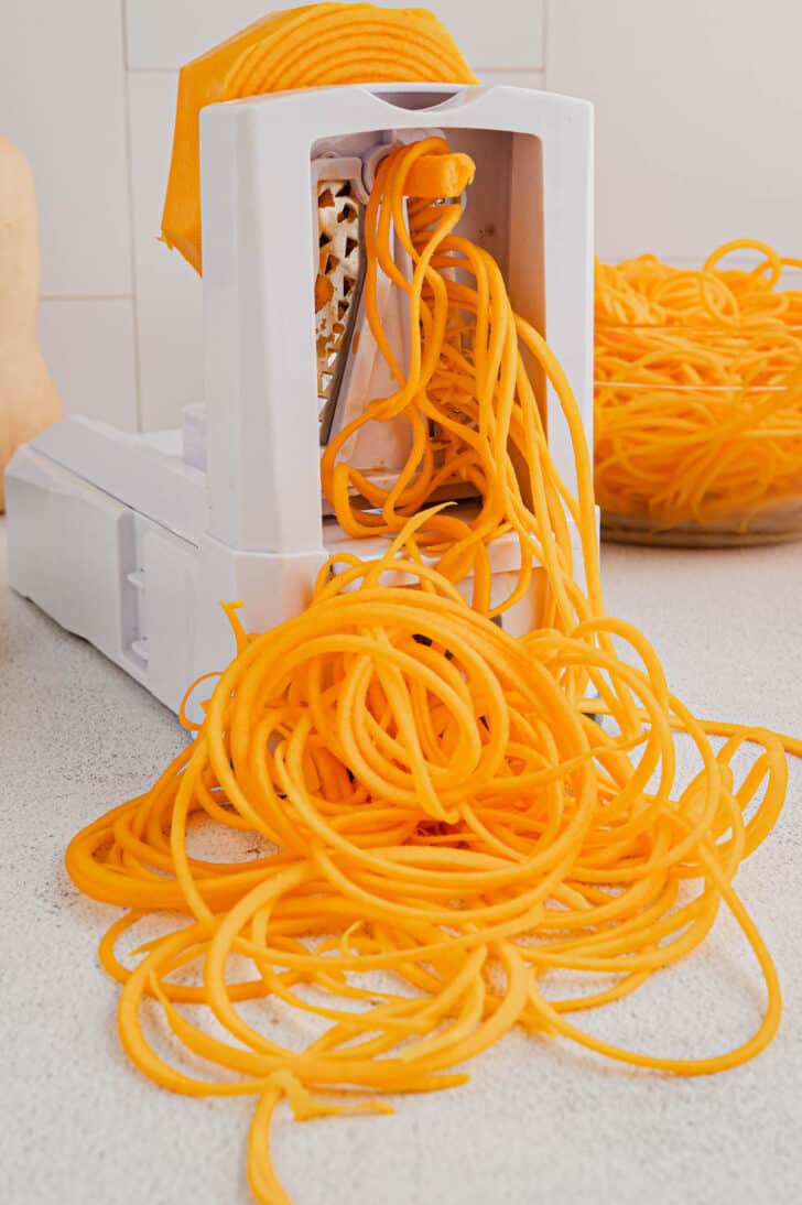 A white spiralizer machine making butternut squash spirals.