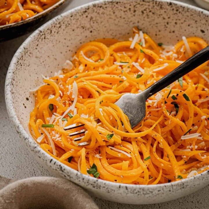 Spiralized butternut squash noodles in a textured bowl with a black fork digging into them.