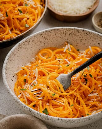 Spiralized butternut squash noodles in a textured bowl with a black fork digging into them.