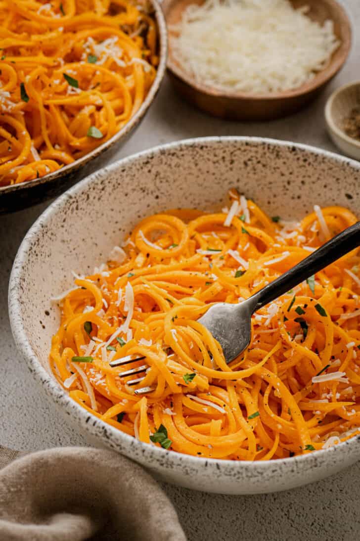 Spiralized butternut squash noodles in a textured bowl with a black fork digging into them.