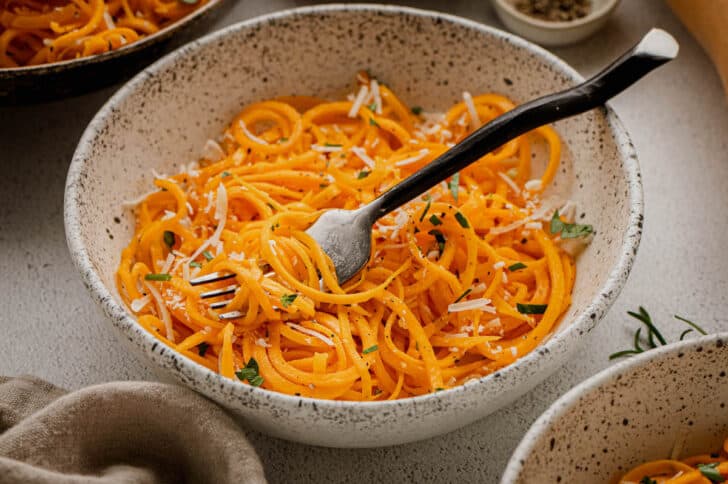 Butternut squash spaghetti in a textured bowl with a black fork digging in.
