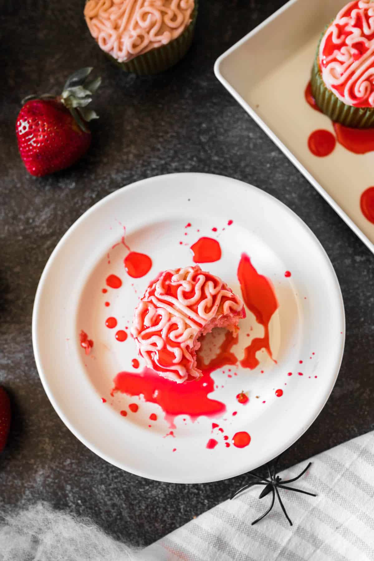 Easy Halloween decorated cupcakes piped with frosting to look like a bloody zombie brain, on a white plate, with a bite taken out of it.