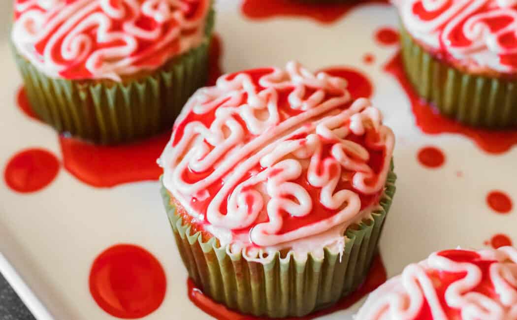 Halloween cupcakes piped with frosting to look like bloody zombie brains, on a white platter.