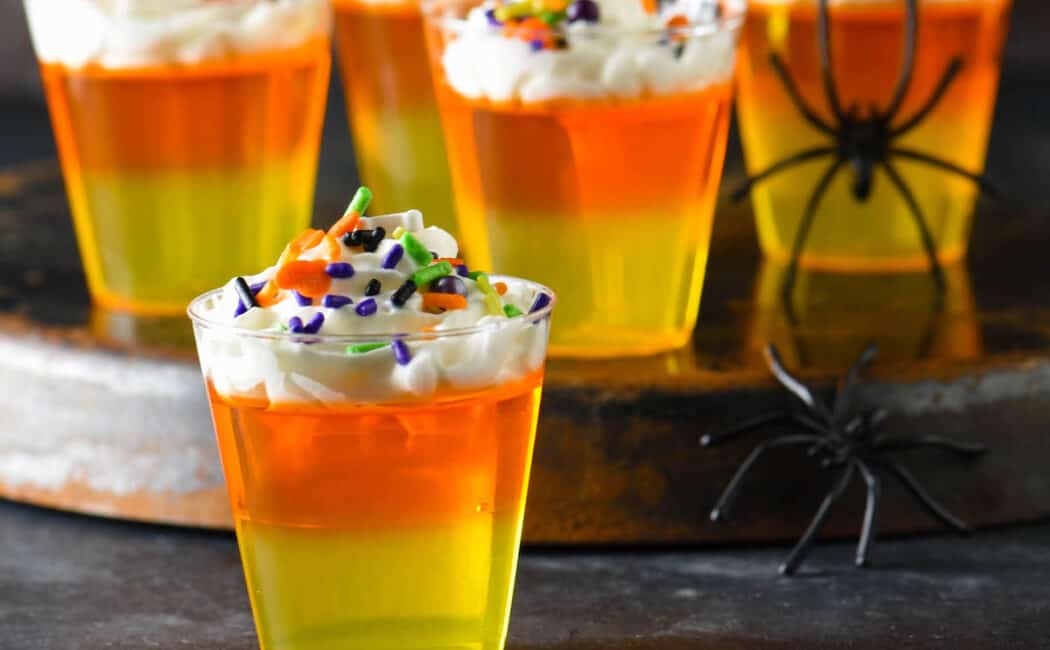 Halloween Jello shots made with layers of yellow and orange Jello and whipped cream, topped with sprinkles.