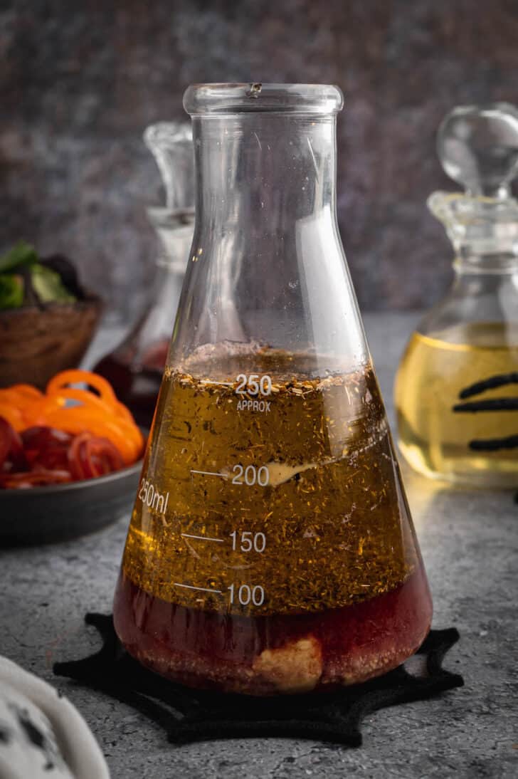 A beaker of salad dressing ingredients, including, oil, red wine vinegar, mustard, garlic and herbs.