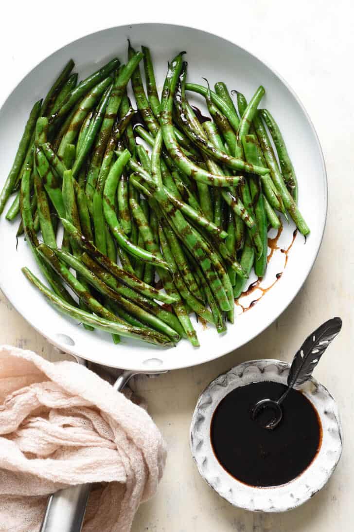 String beans in a white skillet with a dark brown glazed drizzled over them.