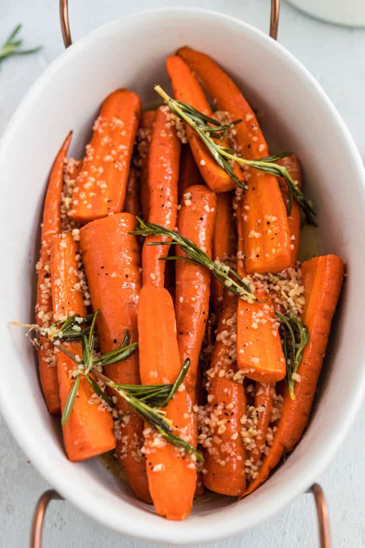 A white ceramic dish filled with roasted glazed carrots garnished with herbs.