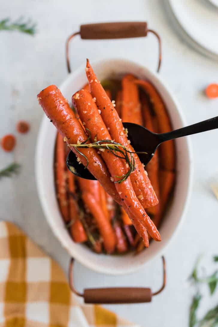 A black spoon lifting some of a honey glazed carrots recipe out of a baking dish.