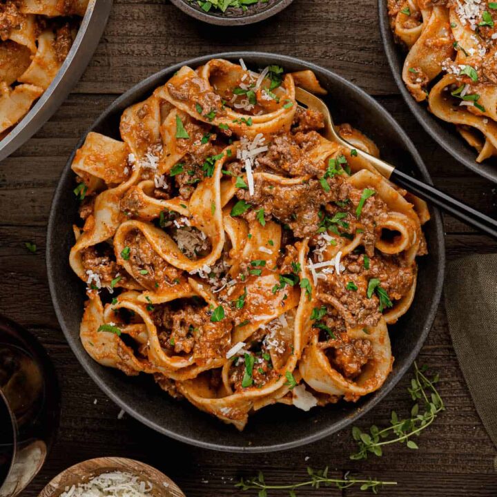 A black bowl filled with lamb bolognese tossed with pappardelle noodles.