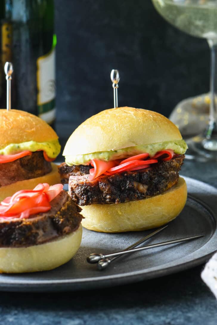 Lamb sliders on small rolls garnished with pickled radishes and pesto mayo, and skewered with decorative silver toothpicks.