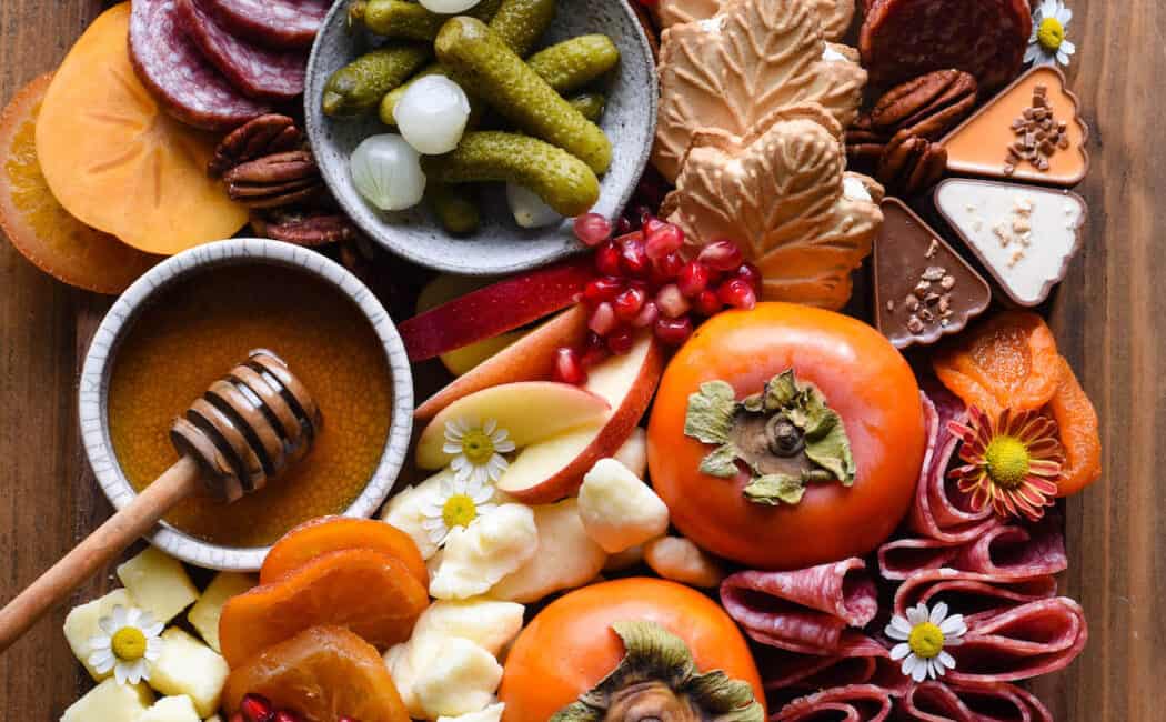 A Thanksgiving charcuterie board, including cured meats, cheeses, nuts, olives, fruit and crackers, arranged on a large wooden cutting board.