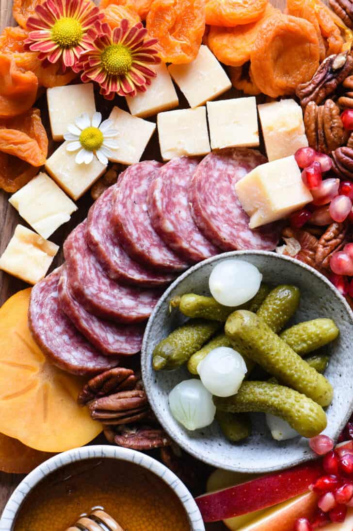 An appetizer tray with salami, cheese, nuts, dried fruit and pickles.