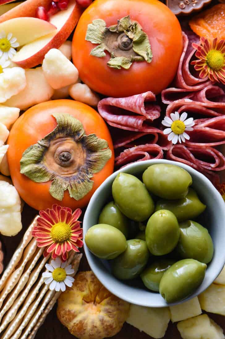 A fall charcuterie board featuring salami, olives, cheese and persimmons.