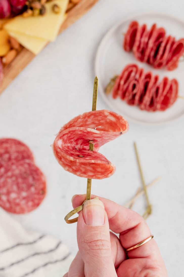A slice of salami folded into quarters and being skewered onto a decorative toothpick.
