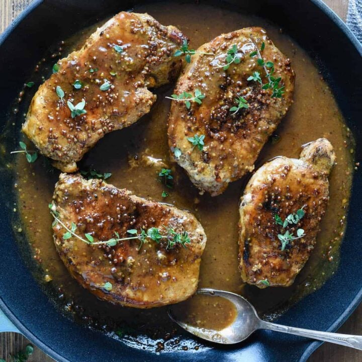 A cast iron skillet filled with honey mustard pork chops, and a spoon to scoop the sauce.