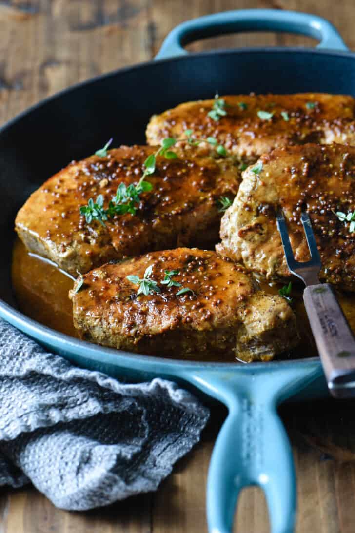 A cast iron skillet filled with honey mustard pork chops, with a fork taking one out.