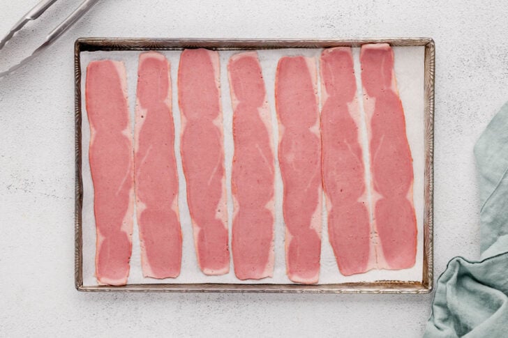 A rimmed baking pan with turkey bacon in the oven ready to be cooked.