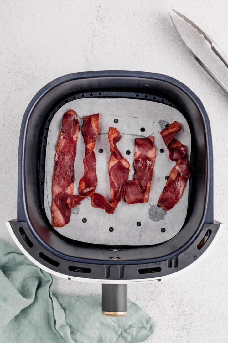 Five slices of turkey bacon in an air fryer basket.