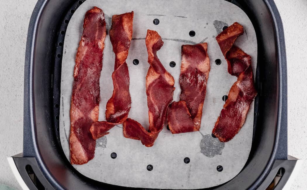 Five slices of turkey bacon in an air fryer basket.