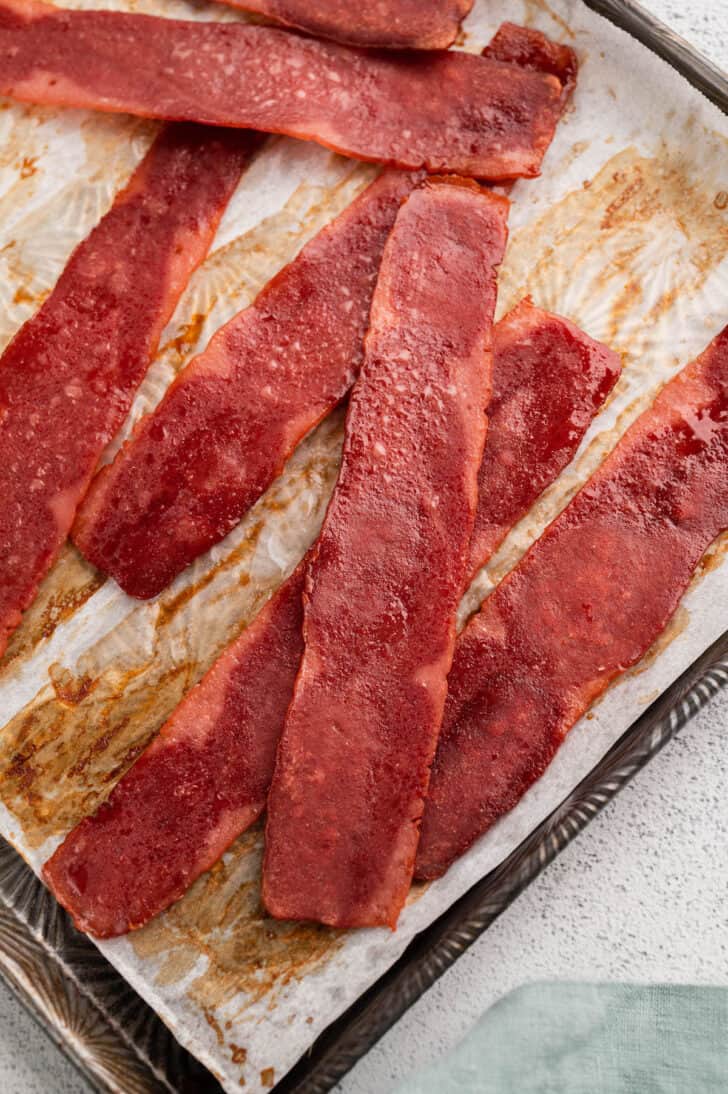 Oven baked turkey bacon slices sitting on top of a rimmed baking pan.