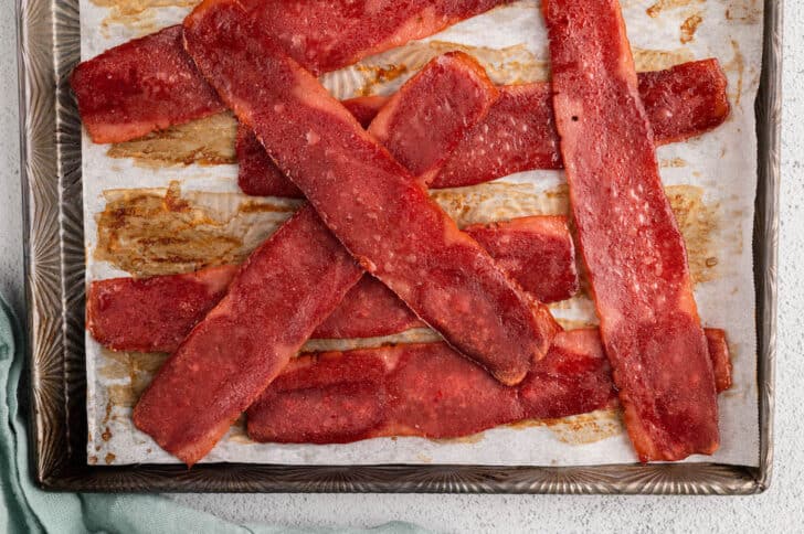 A pile of cooked turkey bacon slices on a rimmed baking pan.