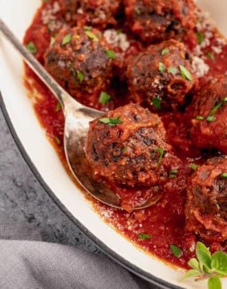 Black bean meatballs smothered in marinara sauce in a baking dish, with a spoon lifting out one bean ball.