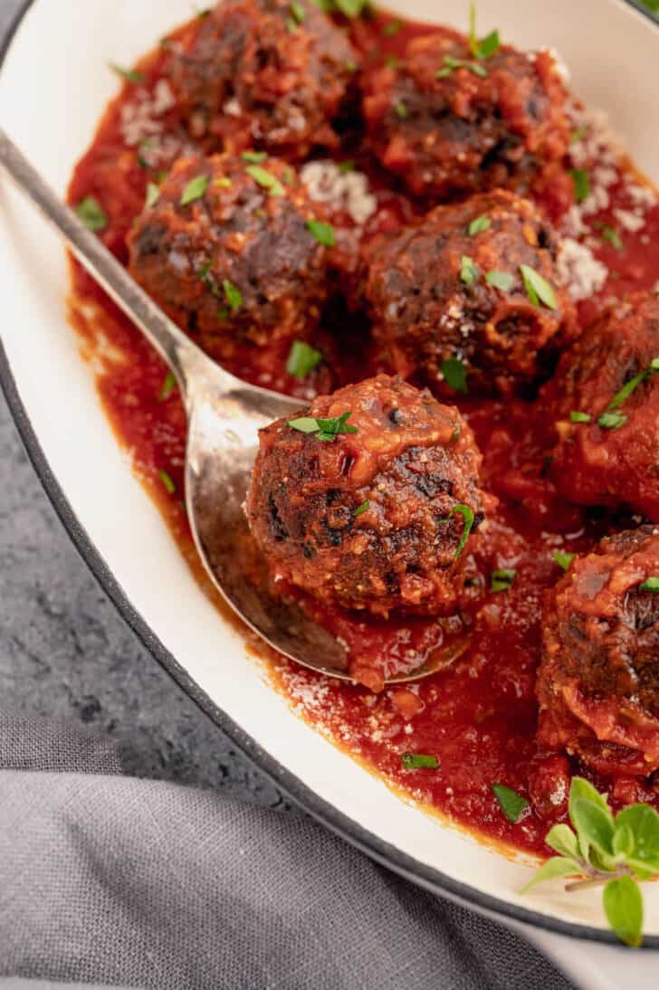 Black bean meatballs smothered in marinara in a baking dish, with a spoon lifting out one bean ball.