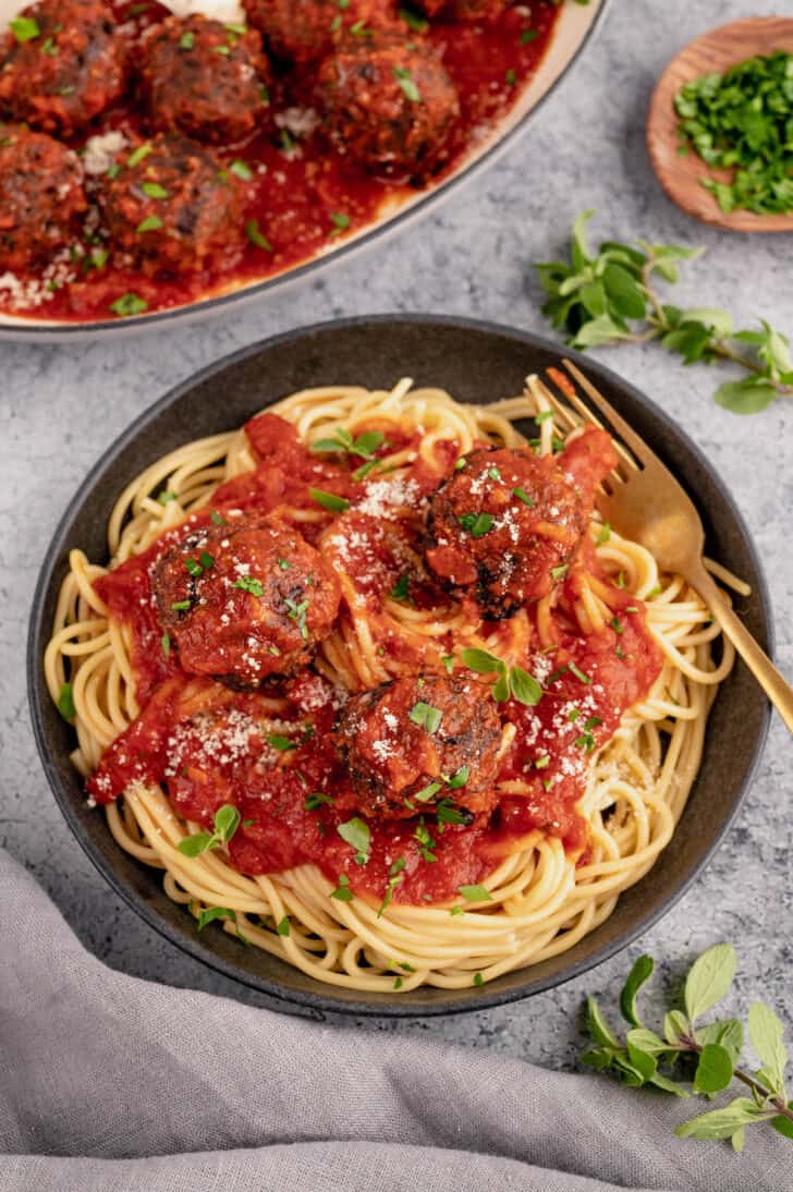 Spaghetti and meatballs in a black bowl with a gold fork digging in.
