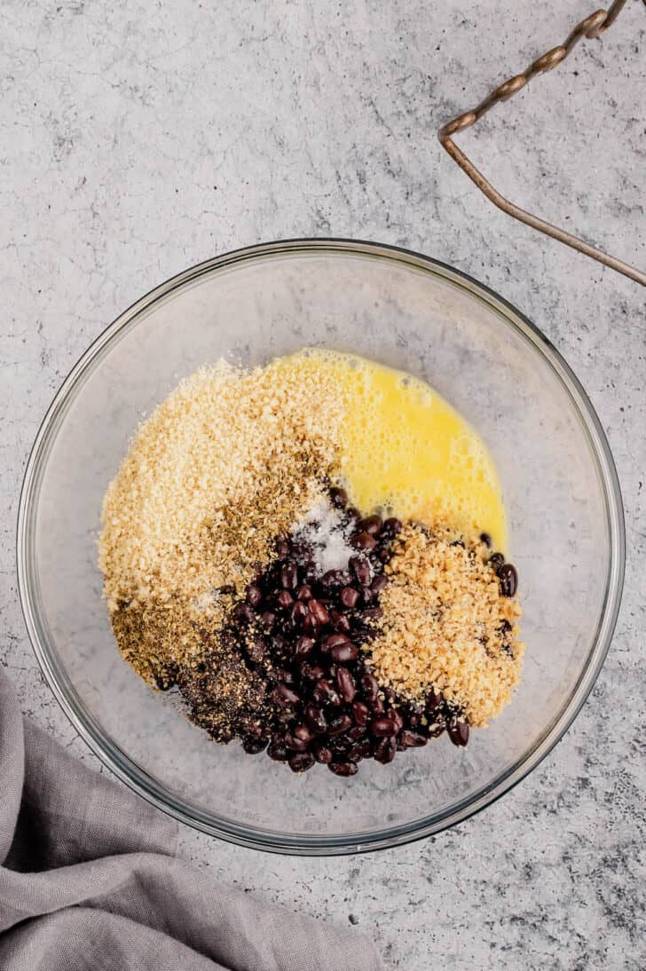 A glass bowl filled with beans, breadcrumbs, chopped walnuts, egg and spices.