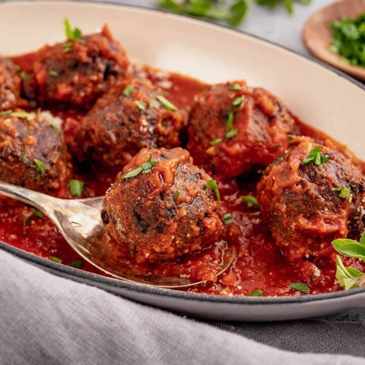 Black bean meatballs smothered in marinara sauce in a baking dish, with a spoon lifting out one bean ball.