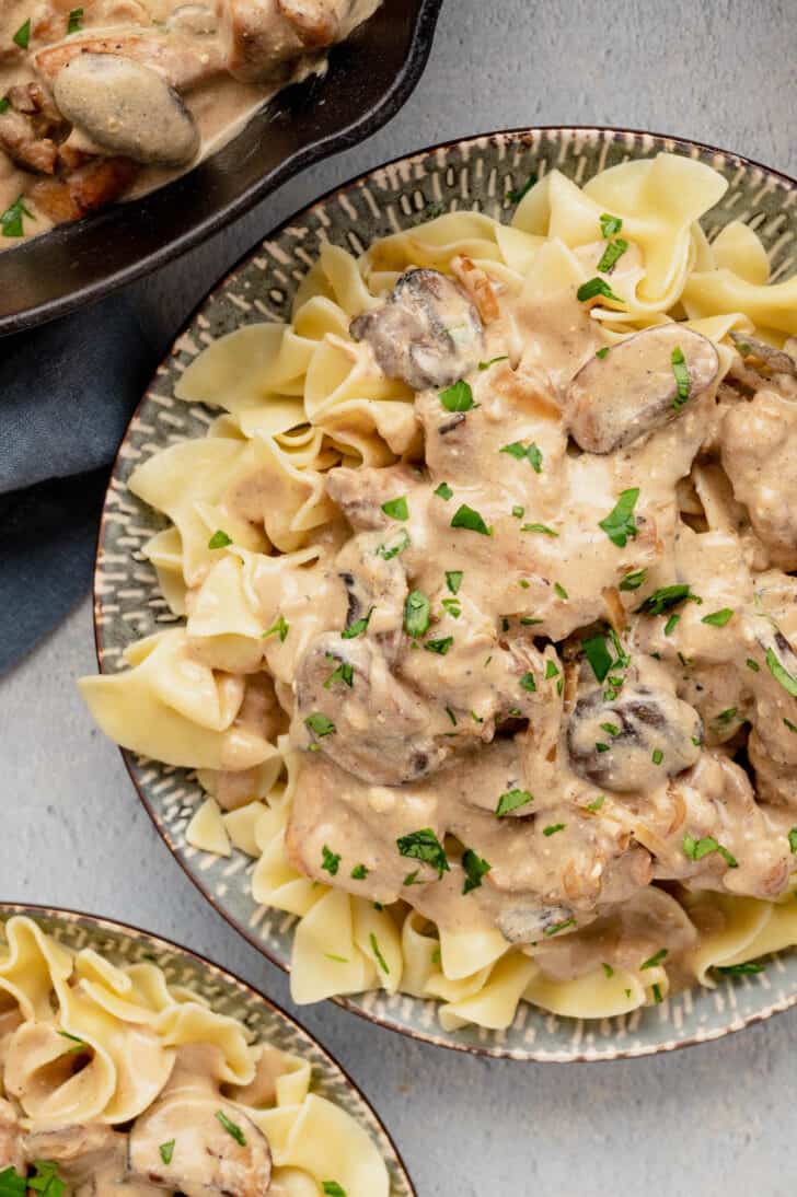 A plate filled with egg noodles topped with chicken stroganoff, garnished with parsley.