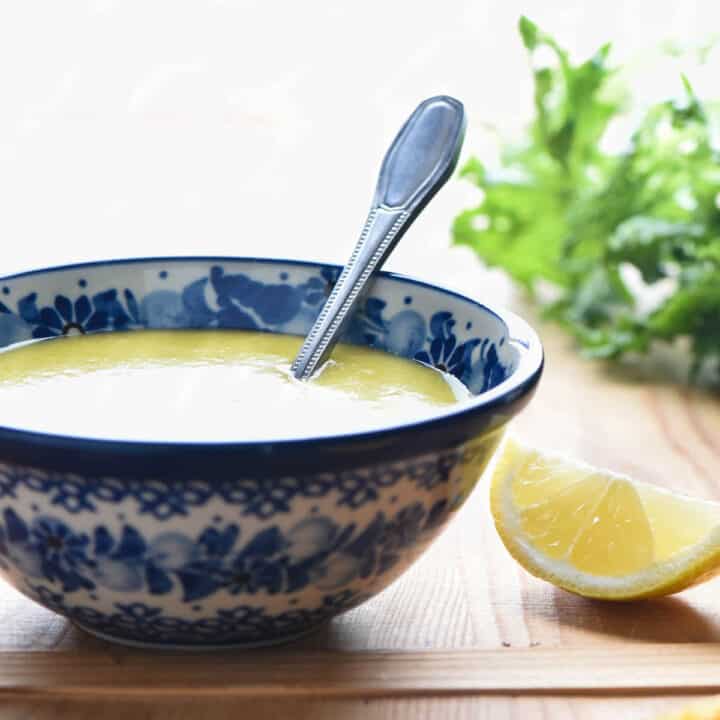 A small painted blue bowl filled with citrus salad dressing with a spoon in it.