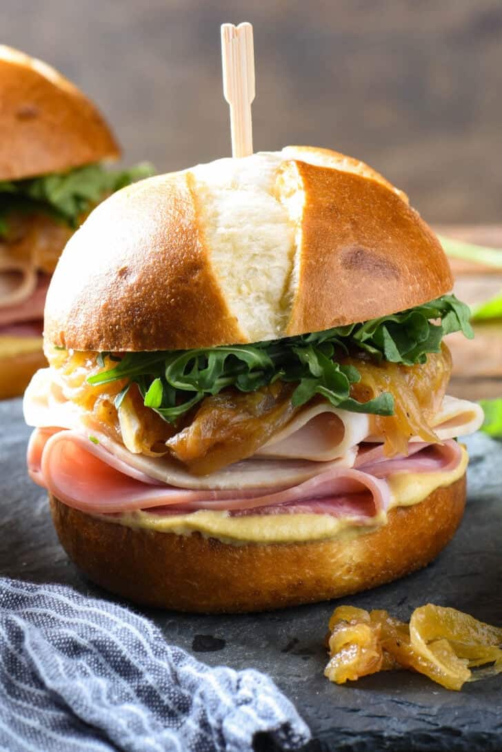 A ham and turkey slider made on a pretzel roll, dressed with arugula, caramelized onions and mustard.