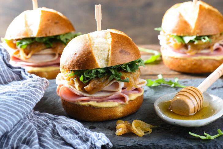 Turkey and ham sliders dressed with arugula and caramelized onions on a slate platter.